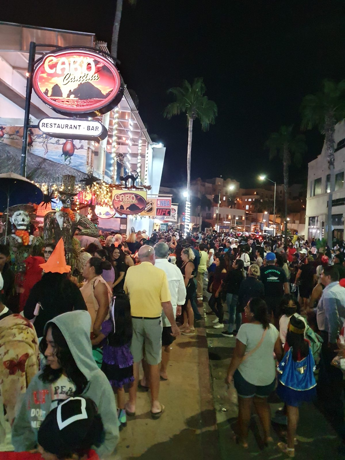 Families and costumed children fill the street outside the illuminated Cabo Cantina sign on Halloween 2022.